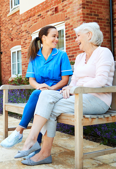 a happy elderly woman sitting on a bench with her caregiver