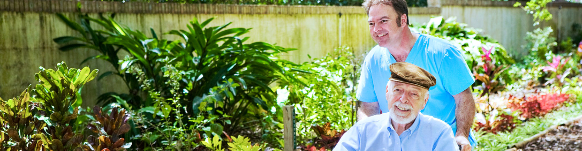 Disabled senior man being pushed through a lovely garden by his nurse.